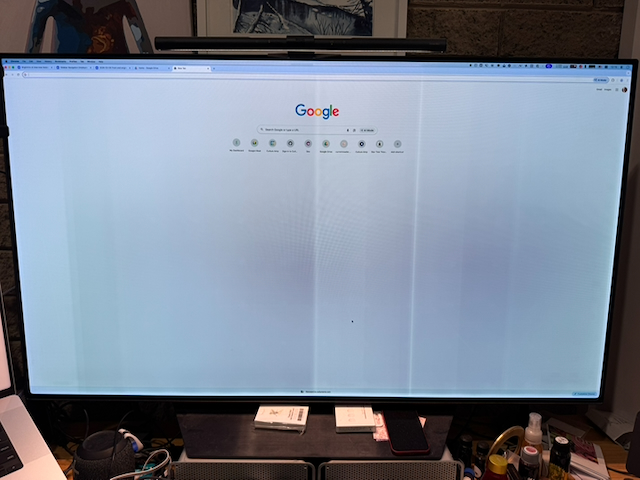 Photo of a large desktop monitor showing the Google home page open in a full-screen browser window. The white background of the web page shows clear signs of burn-in.