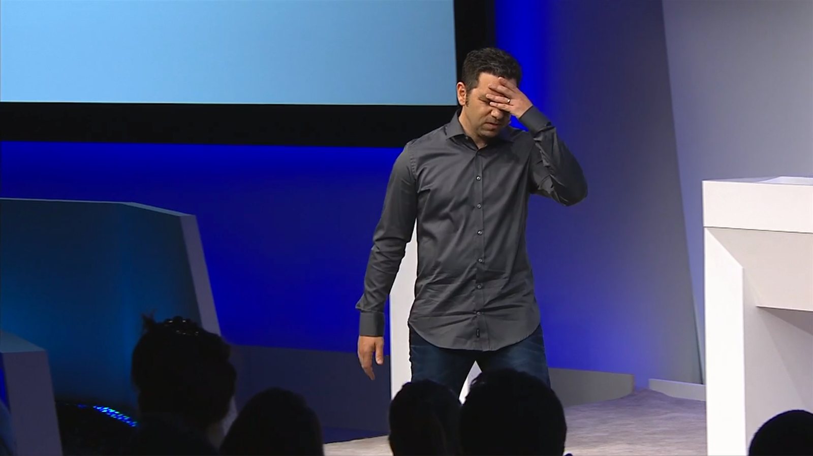 Panos Panay grimaces with his hand on his forehead as he crosses the stage.